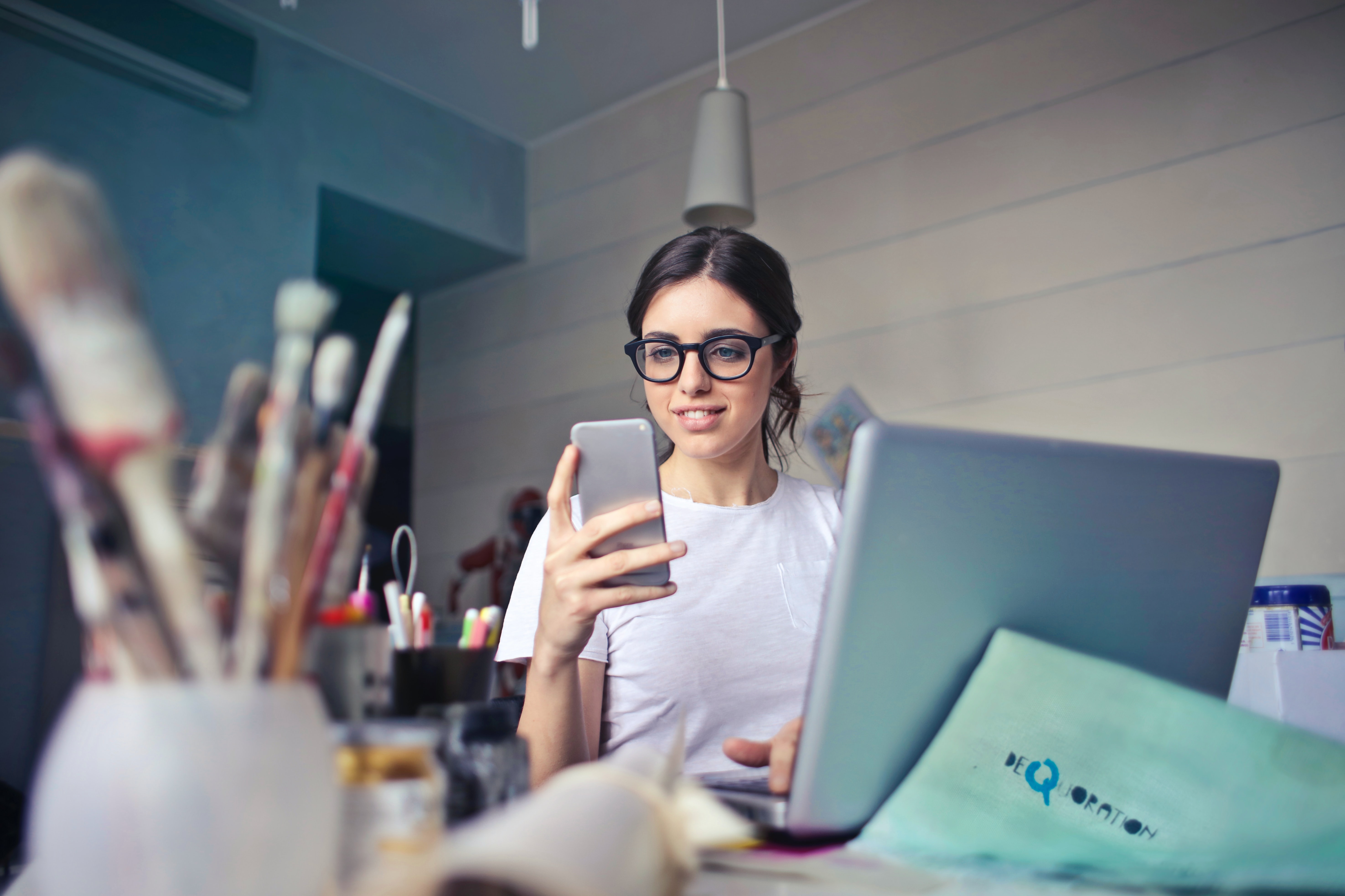 A woman looking sitting at a desk with a laptop and holding a mobile phone